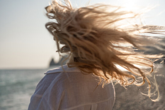 Hair wind beach. Blonde woman's flowing hair blows wildly by the ocean at sunset, evoking feelings of freedom and natural beauty