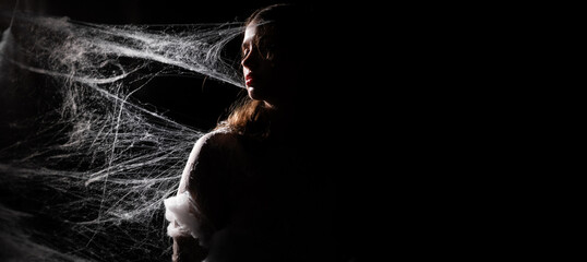 Fine art photo of a young woman wrapped in spider web on black background. Black and white photo. copy space