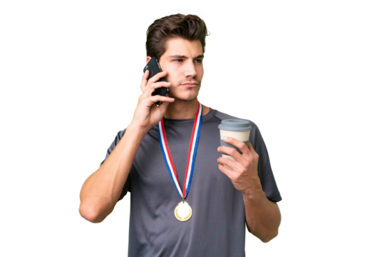 Young caucasian man with medals over isolated background holding coffee to take away and a mobile - Powered by Adobe