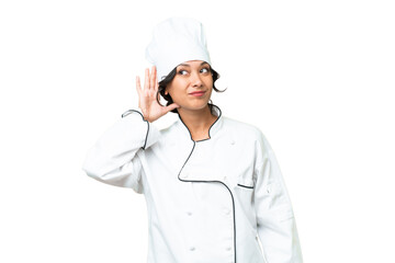 Young chef Argentinian woman over isolated background listening to something by putting hand on the ear