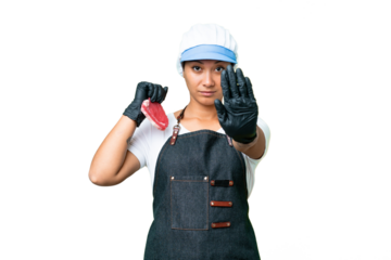 Butcher woman wearing an apron and serving fresh cut meat over isolated chroma key background making stop gesture