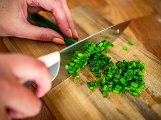 Woman cutting chives on wooden board, close-up of hands