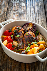 Roasted chicken drumsticks and vegetables in baking dish on wooden table