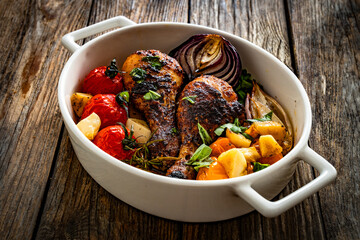 Roasted chicken drumsticks and vegetables in baking dish on wooden table