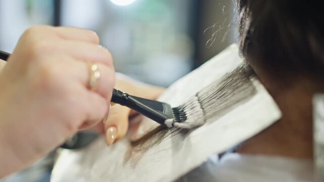 Close up of professional hairdresser applying hair dye during bleaching process in modern salon showing beauty treatment hair care and hairstyle transformation
