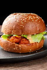 Crispy chicken sandwich with lettuce, tomato, pickles, and sauce on a sesame brioche bun, served on a black plate. Close-up food photo for menu, advertising, or culinary content.