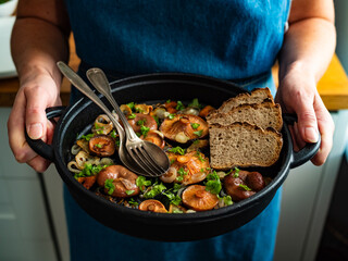 Woman holding frying pan with fried saffron milk cap mushrooms, close-up