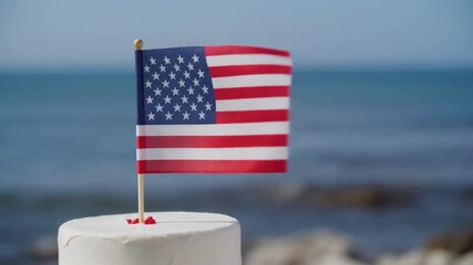 American flag atop a white cake with ocean backdrop, capturing the spirit of summer patriotism. - Powered by Adobe