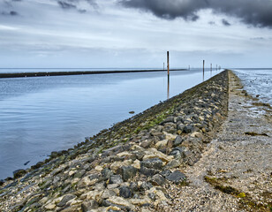 Navigating channel through the north sea mudflats at low tide with a rock-strewn dike leading the way
