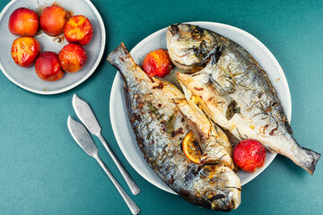 Baked dorado fish with plums served on a plate.