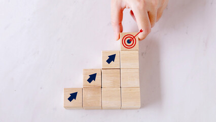 Hand placing the final wooden block with a bullseye target icon on top of a staircase, symbolizing business goal achievement, strategy, and career success.