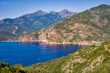 view from the mountains of Porto Ota Bay in the Gulf of Porto and the red cliffs, with calm, deep blue sea, sunshine, and blue skies