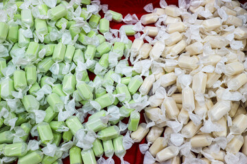 Traditional Thai Toffee in green (Pandan) and white (Coconut Cream) flavors. Wrapped sweets on a red surface. A popular street candy showcasing tropical Asian confectionery and local flavors.