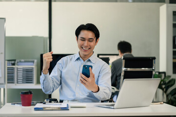 Obraz premium Successful business man, excited young man Keeping up arms and showing positive emotions, happy working in modern office on smartphone.