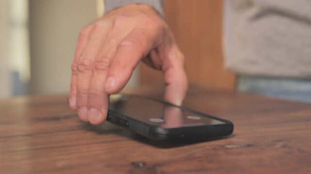 Male picking up phone displaying incoming call on the screen from the wooden table at home