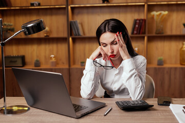 Woman with glasses massaging head at laptop showing migraine and computer stress at work