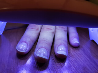 The procedure for manicuring nails, polishing, drying. A woman dries her nails under an ultraviolet lamp. Manicure, nail drying, nail polish.