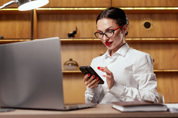 Businesswoman using smartphone at laptop for messaging and app notifications