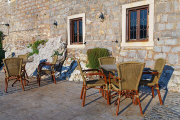 cozy outdoor cafe or restaurant located on embankment of Petrovac city, Montenegro, tables and chairs against the background of a stone wall of an old building