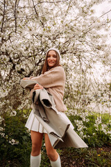 A girl in a light sweater and skirt against a backdrop of a blossoming tree 7269.
