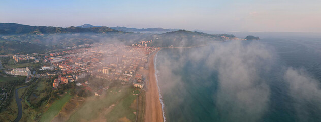 Panoramic drone view of clouds above Zarautz town on summer sunrise. Basque Country, Spain.
