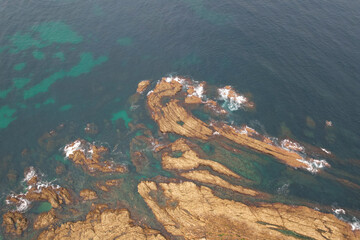 Top aerial view of rocks in the sea on sunny summer day. Pechon, Cantabria, Spain.
