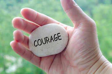 Hand holding a white stone with COURAGE text engraved on it, embodying life purpose of bravery and...