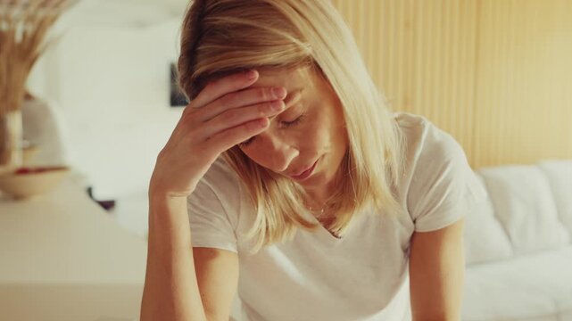 Woman Holding Head Feeling Unwell in Bright Living Room