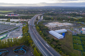 Aerial view of the M60 motorway near the Trafford area with surrounding fields and industrial sites at sunset.