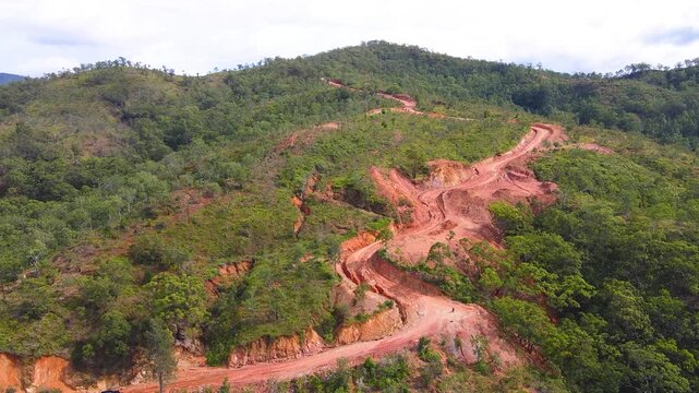 An aerial view of a challenging red dirt road along a ridge in the rural hills of Aileu, Timor-Leste. Poor road conditions highlight infrastructure challenges in remote areas.