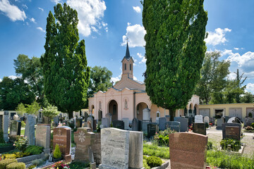 Wunderschöne Kapelle mit vielen Grabsteinen und hohen Bäumen auf einem Friedhof in Rosenheim  © Blende8