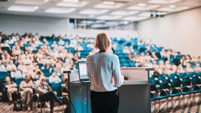 Female speaker giving a talk on corporate business conference. Unrecognizable people in audience at conference hall. Business and Entrepreneurship event