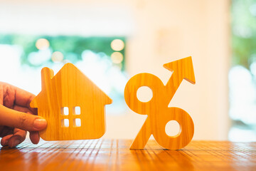 Wooden house model and percentage symbol with upward arrow represent rising interest rates, real estate investment, mortgage loan costs, and financial growth in housing market trends.