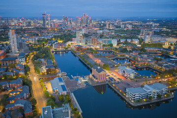 Aerial view of Salford Quays waterfront at twilight with reflections on calm water and Manchester skyline beyond.