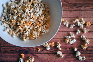 white bowl of popcorn on a wooden table with scattered popcorn
