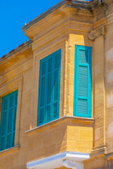 Corner of colored stone building is visible in the sun. Windows with bright turquoise shutters. Detailed view of traditional window shutters in a striking teal color against weathered stone