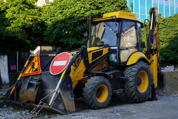 Construction equipment parked on a city street during the day next to trees and a building