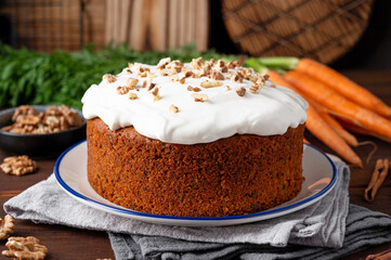 Carrot cake with cinnamon, walnuts and cream cheese frosting on a plate on a dark wooden background. Rustic style. Copy space.