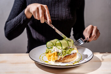 Woman cutting avocado toast with scrambled eggs and zucchini