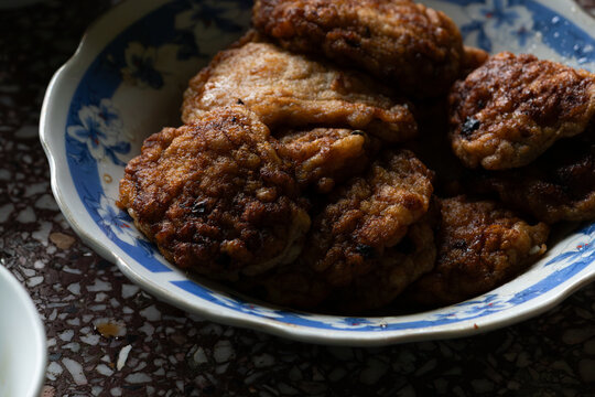 A moody still life of Vietnamese fried ragworm patties (Cha Ruoi), a traditional delicacy, in a bowl with dramatic Chiaroscuro lighting.