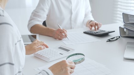 Groupe of accountants collaborating on financial analysis, using a magnifying glass, calculator, and laptop to ensure data accuracy. Audit and taxes