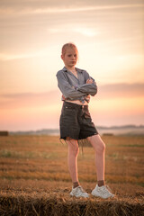 Young woman in casual attire stands in a field at sunset, surrounded by hay bales, showcasing a serene atmosphere and natural beauty with vibrant colors