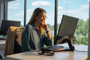 Young professional businesswoman smiling, finding work satisfaction while using a desktop computer...