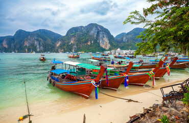 Thailand. Longtail boats on the beach at Phuket. Famous Koh Phi-Phi Don island with white sand beach and turquoise water under blue sky. Vacation holidays summer background in Phuket, Thailand.