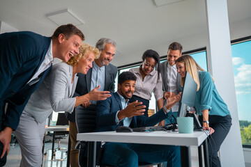 Multigenerational business professionals gathering around a computer screen, celebrating...