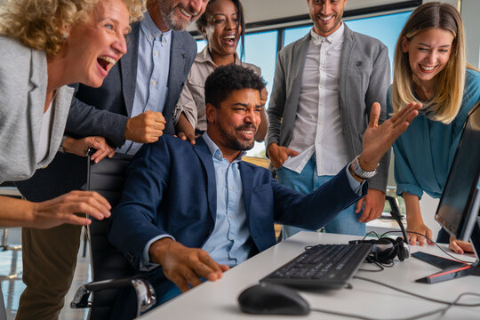 Diverse business professionals feeling happy collaborating and celebrating a great result at the office, looking at a computer monitor and sharing a moment of achievement and teamwork