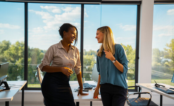 Diverse businesswomen colleagues engaging in a friendly conversation and laughing in a modern office environment, fostering positive communication and teamwork