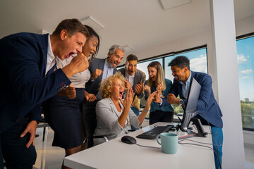 Diverse business team in an office cheering over a computer screen after reaching a major financial milestone, capturing teamwork, triumph, celebration, and shared success