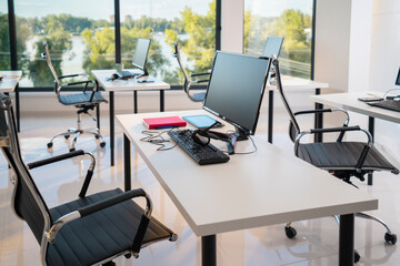 Contemporary open plan office interior featuring multiple workstations with computers, keyboards, and headphones, overlooking a scenic river and lush green landscape through large windows