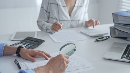Fototapeta premium Groupe of accounting professionals analyzing financial documents, checking spreadsheet details with calculator and magnifying glass. Audit and taxes concept